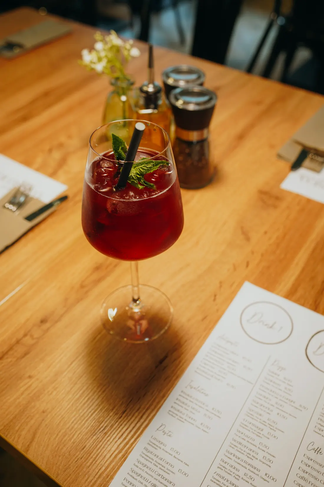 Roter Aperitif mit Minze auf dem Holztisch, daneben die Getränkekarte
