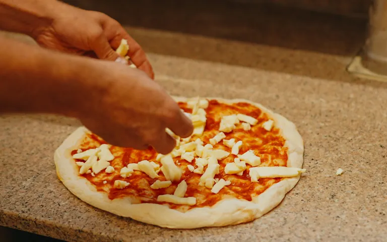 Eine Hand verteilt Käse auf einer Pizza mit Tomatensoße