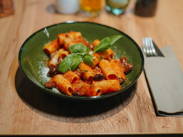 Rigatoni mit Tomatensoße, Oliven und Basilikum in einer grünen Schale