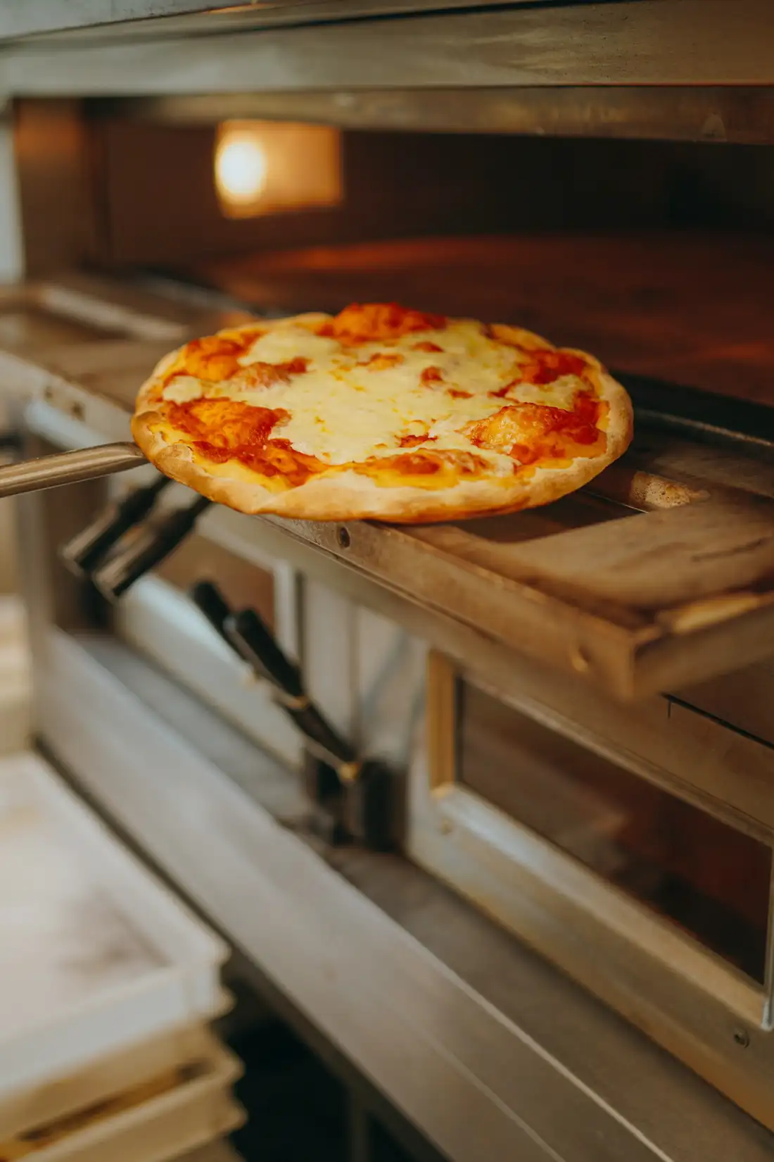 Eine Pizza kommt auf dem Schieber aus dem Steinofen
