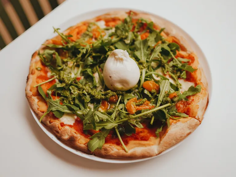 Pizza mit Burrata, Rucola, Tomaten und Pesto auf einem weißen Teller