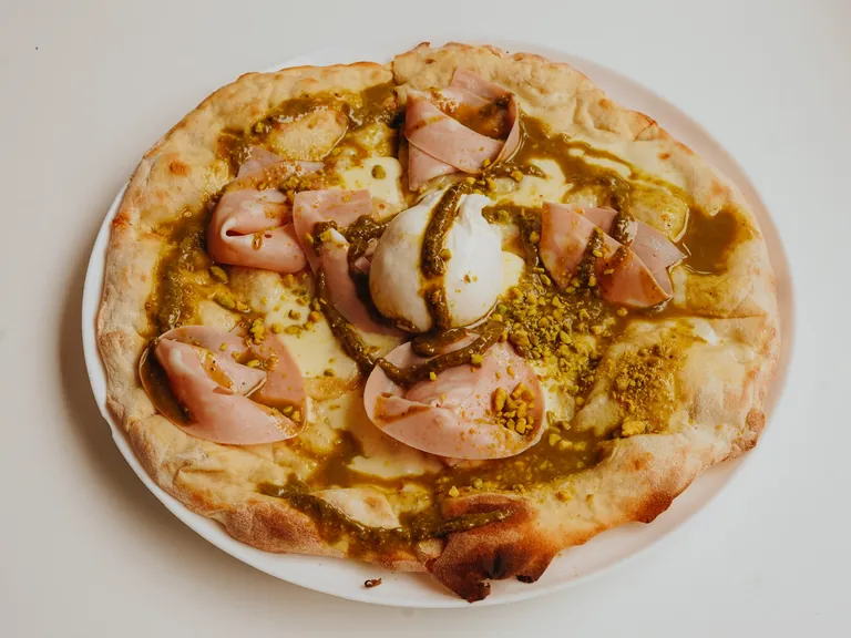 Pizza mit Mortadella, Burrata und Pistazienpesto auf einem weißen Teller