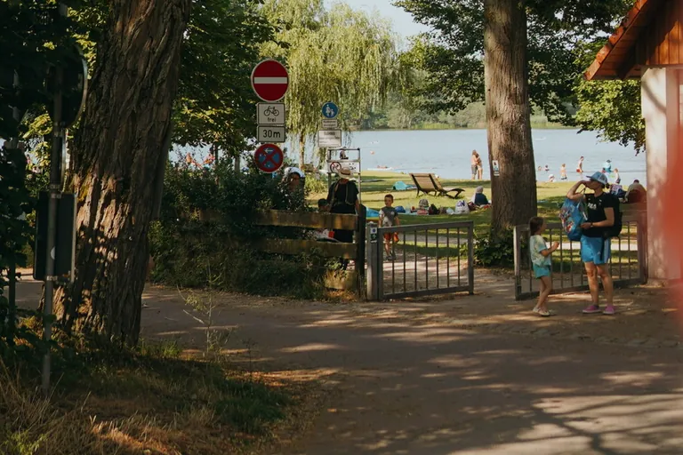 Der Weg zum Dechsendorfer Weiher: ein Tor zwischen Bäumen, dahinter die Liegewiese und das Wasser