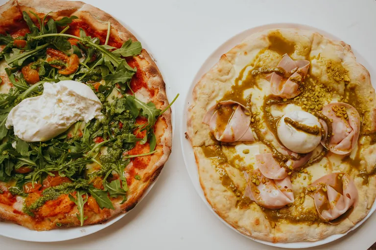 Zwei Pizzen von oben: links Burrata, Rucola und Pesto, rechts Mortadella, Burrata und Pistazie